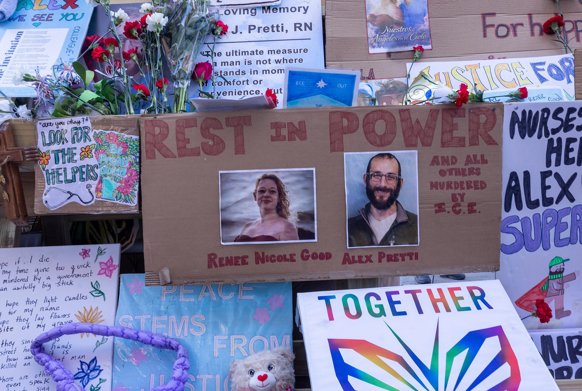 A memorial display honoring Renée Nicole Good and Alex Pretti features a large cardboard sign reading 'Rest in Power' with their portraits surrounded by flowers and messages.