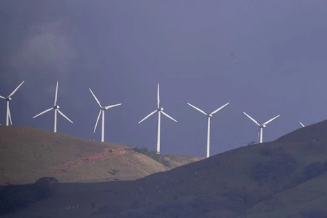A row of wind turbines along a hillside ridge under a stormy sky