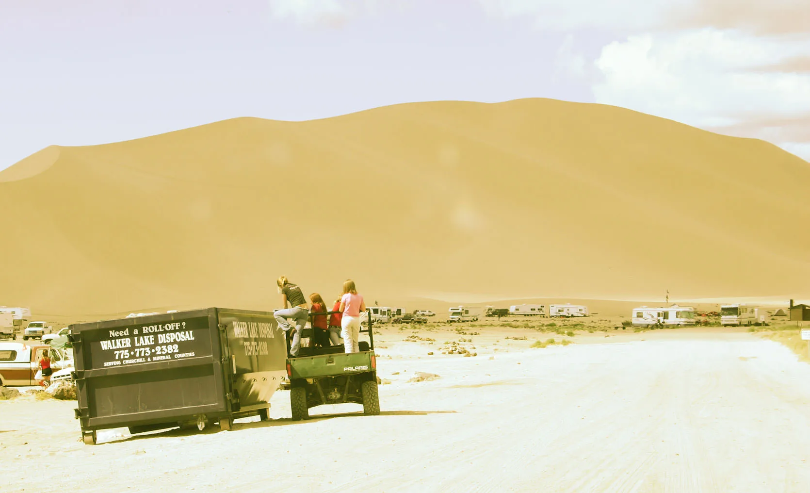 A recycling dumpster and truck in front of the towering sand of Sand Mountain, Nevada.