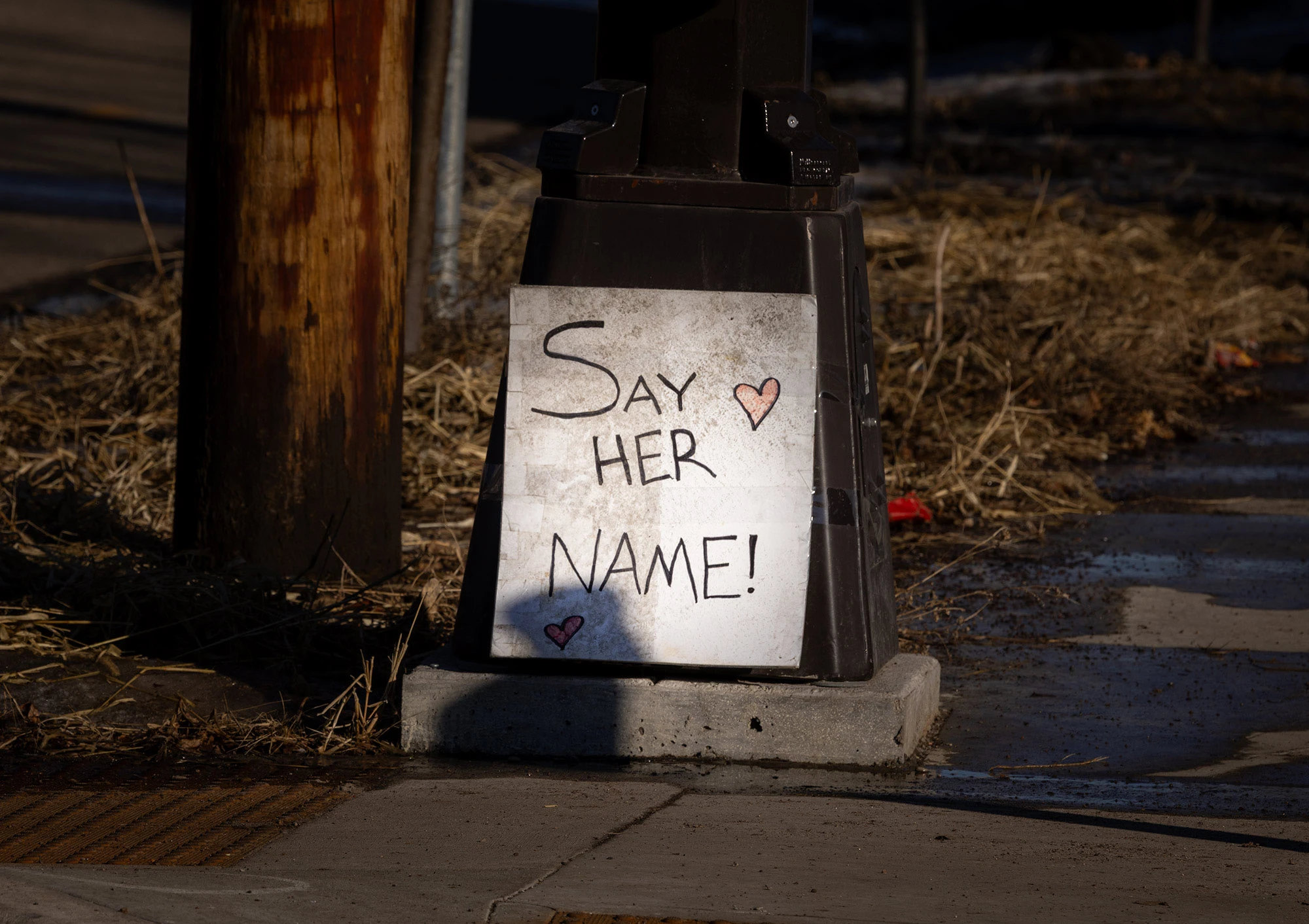 A hand-made sign leaning against a lamp post in south Minneapolis reads 'Say Her Name,' placed near the site where Renée Good was fatally shot by an ICE agent.