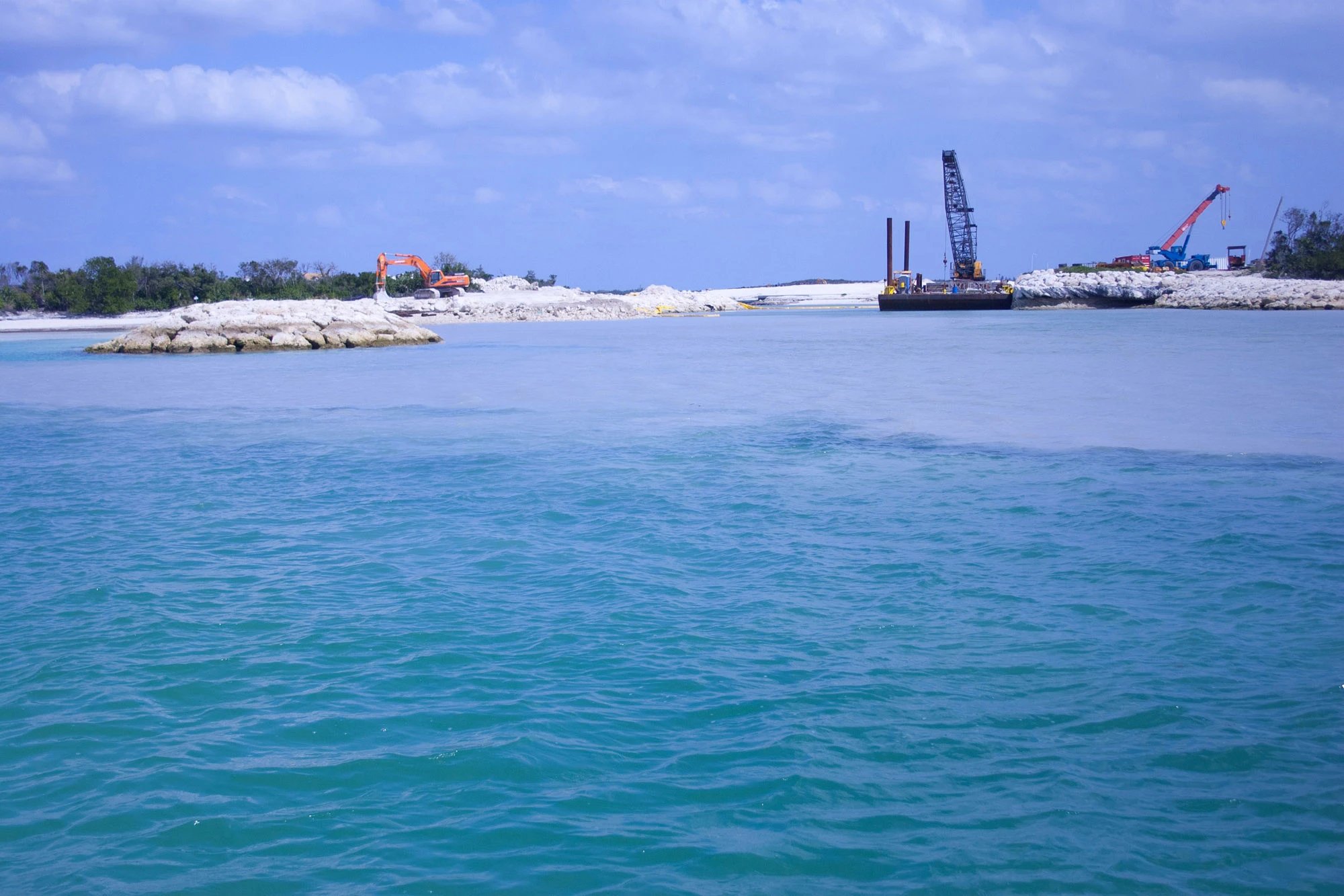 Silt leaching from a construction site directly into the ocean at Baker's Bay, past a protective berm that visibly is not containing it, an image of exactly the kind of unstopped, recurring violation the reports document without consequence.