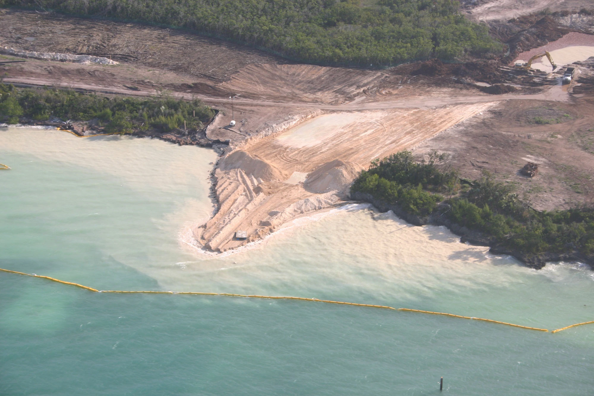 Silt and sediment leaching into the water off Baker's Bay, visibly clouding the sea past a floating protective berm that is failing to contain the sediment plume before it reaches the coral reef.