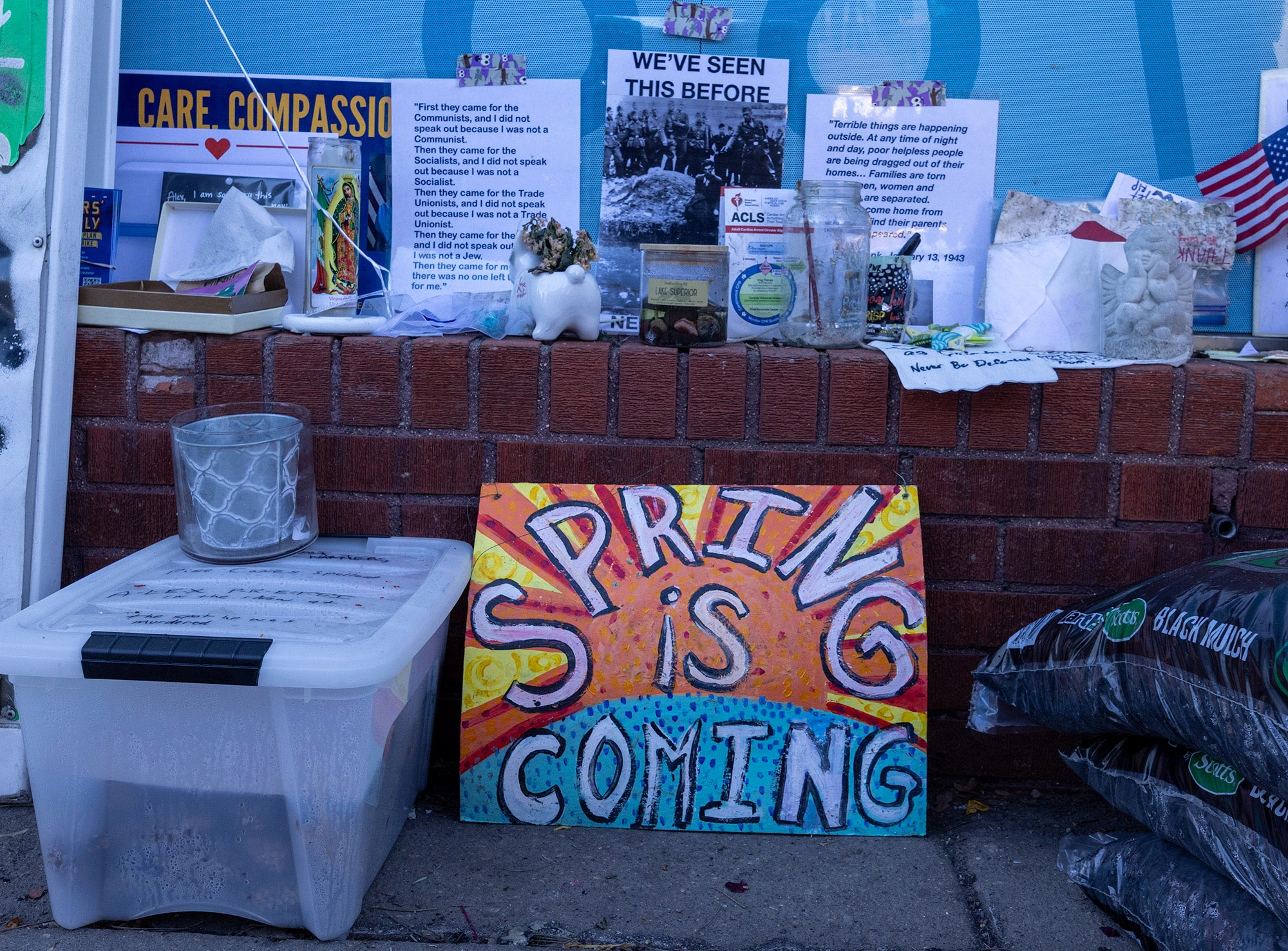 A colorful sign reading 'SPRING IS COMING' sits at the Alex Pretti memorial in Minneapolis alongside candles, candles and protest posters during ongoing demonstrations against federal immigration enforcement.