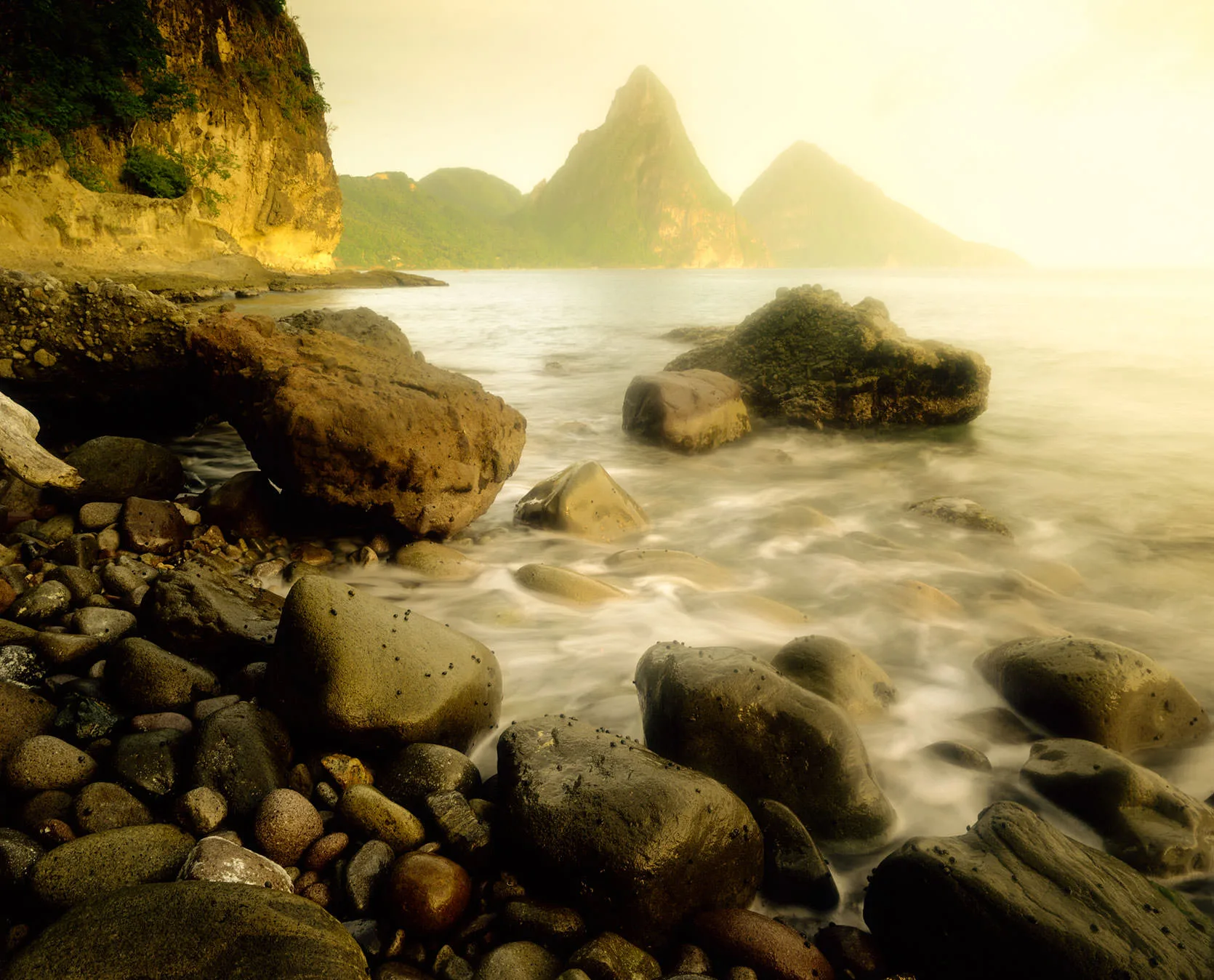 Rounded rocks on the shore near Anse Chastenet, with the Pitons rising through the mist, St. Lucia.