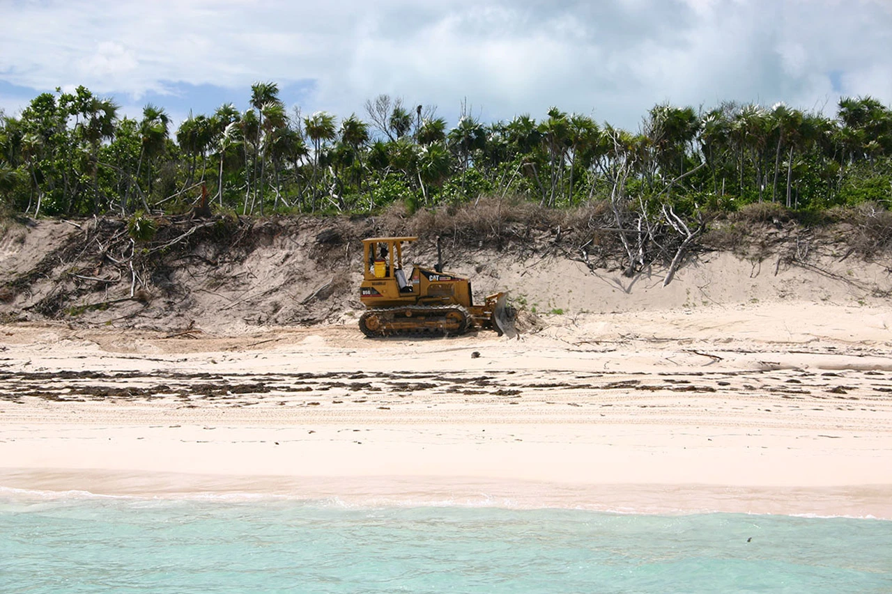 A caterpillar tractor operating directly on the beach at Baker's Bay, reshaping the dune system that faces Great Guana Cay's reef and that the coastal buffer zone was meant to protect.