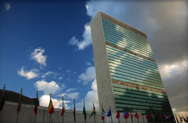 The United Nations headquarters tower in New York, with a row of flags at its base.