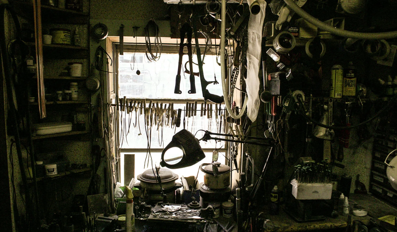 A dim, densely cluttered workshop in Austin, Nevada, tools, wire and jars crowding every wall around a bright window
