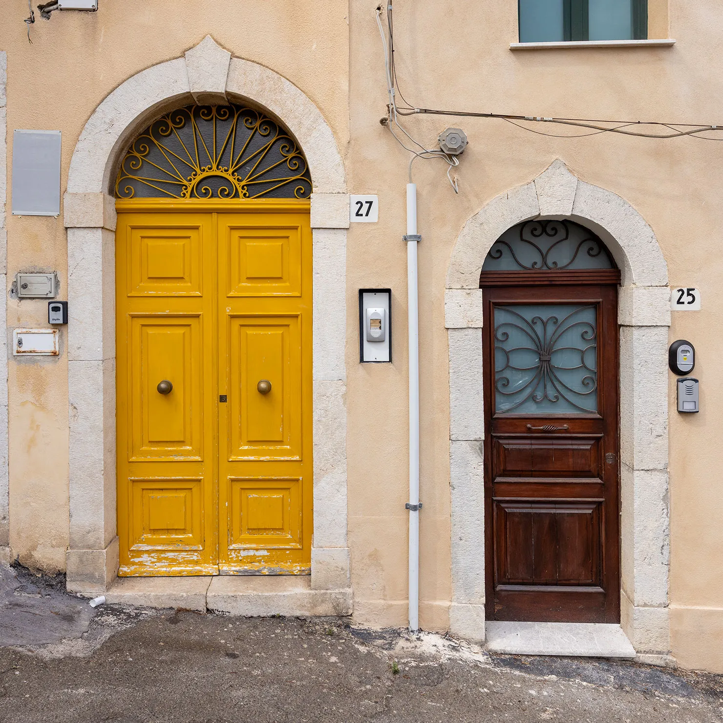 Sunflower-yellow door and dark wooden door in neighboring arched stone doorways in Lipari, Aeolian Islands, Sicily.